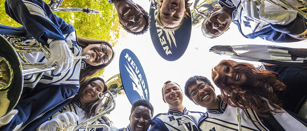 Members of the marching band in full silver and blue uniforms looking down into the camera