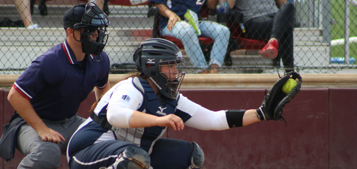 Amanda Nicholas playing catcher in a softball game with a ball in her glove.