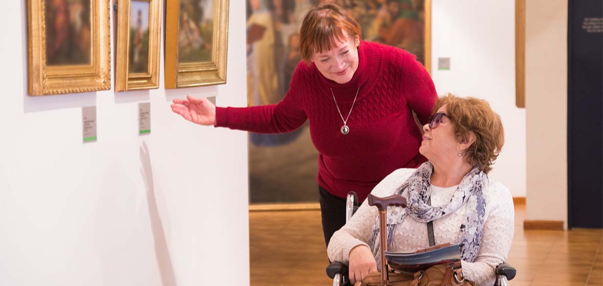 A helper from Sanford Center for Aging assisting a woman in a wheelchair as the go through a museum together