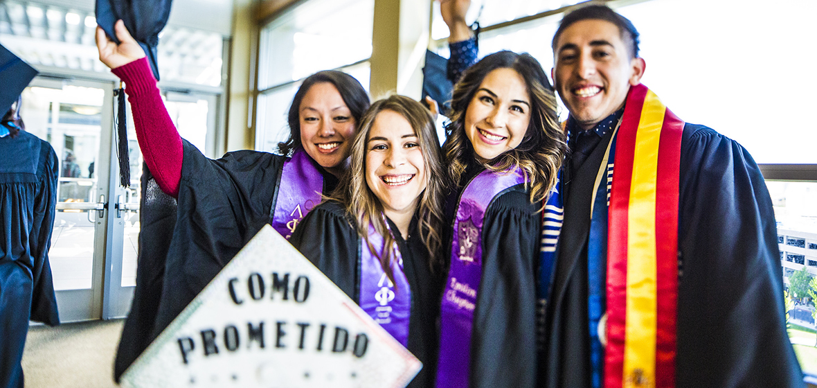 Four students celebrate at Commencement. One student's graduation cap says, "Como Prometido BSN"