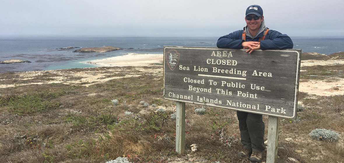 Chris Jazwa standing behind Channel Islands State Park sign with ocean in background