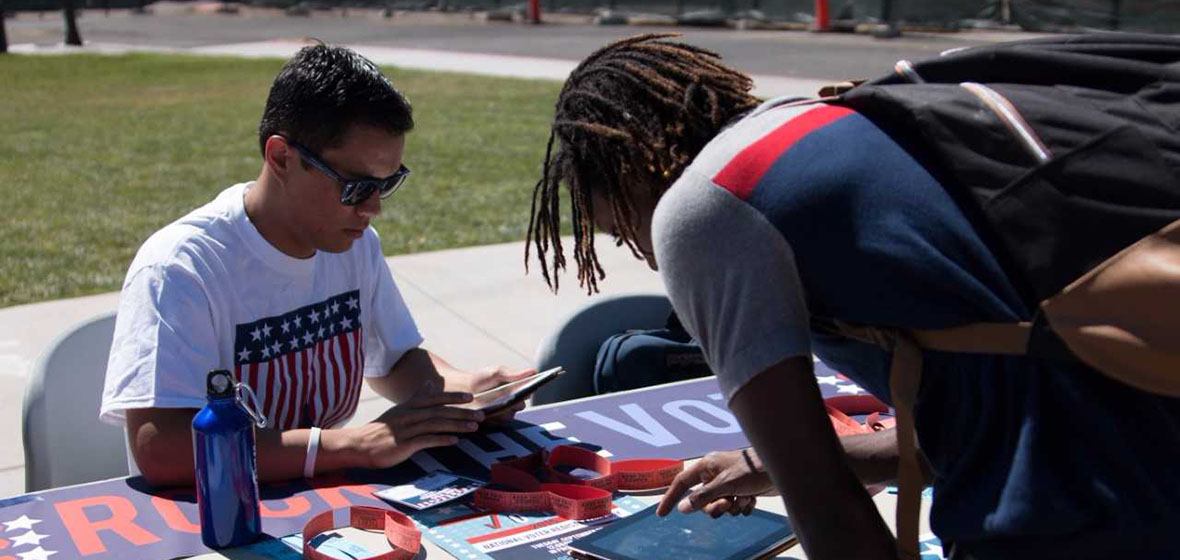 two college students at a voting table, one is registering to vote