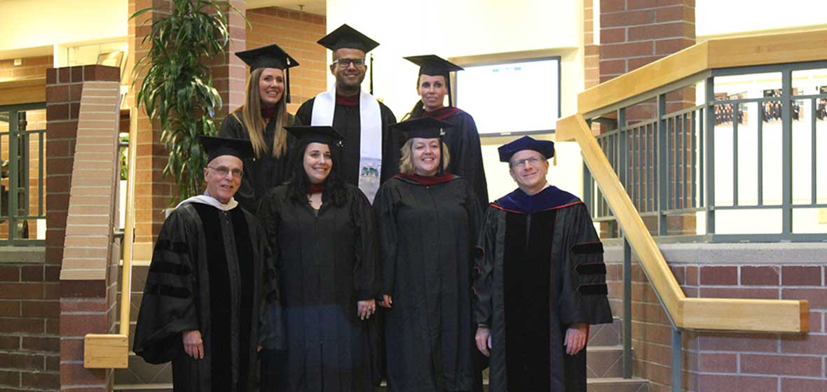 A group of people in graduation robes stand on a set of stairs. 