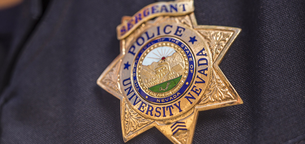 Gold police badge with Sergeant, Police, and University Nevada written on it.  The Great Seal of the State of Nevada with the seal in the middle of the badge.