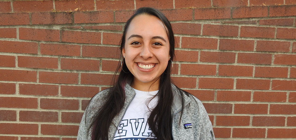 Alexis Duenas smiling in front of a red brick wall. 