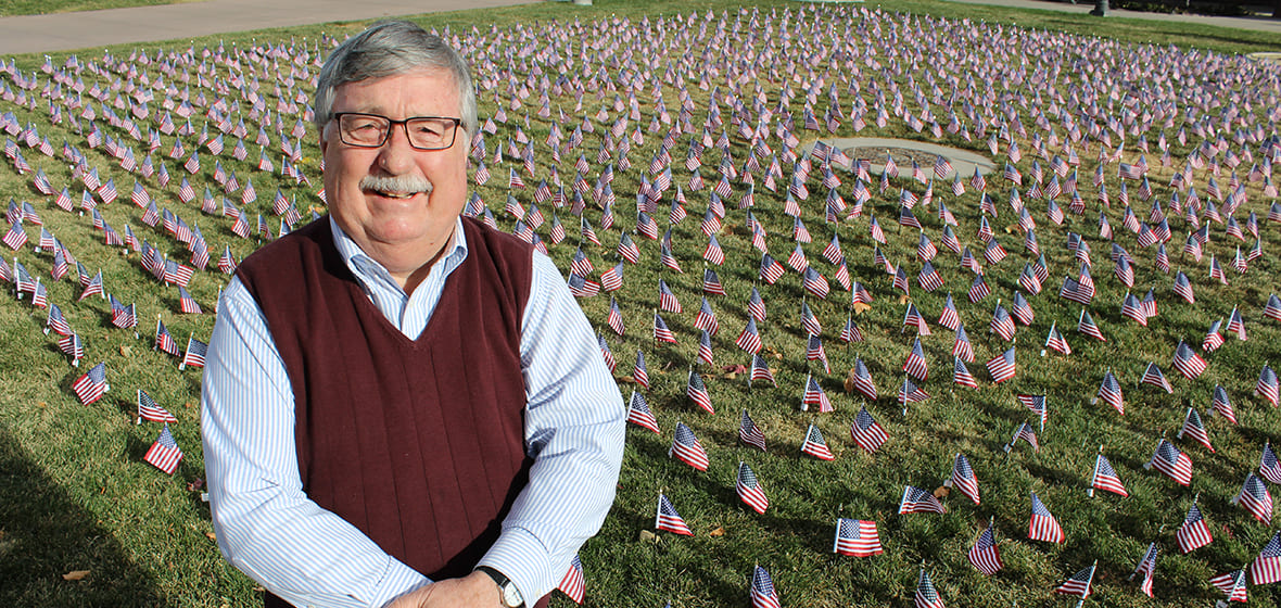 Professor Bob Felton poses in front of American flags decorating the lawn in front of the Joe Crowley Student Union. 