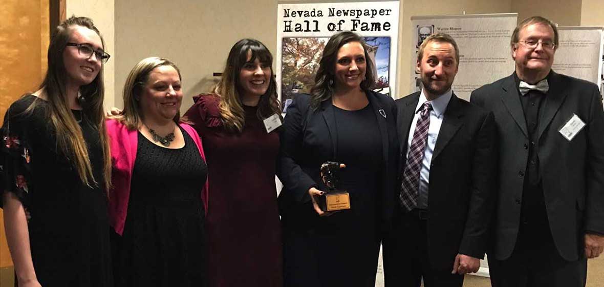 A group of people pose together. One of them is holding an award. 