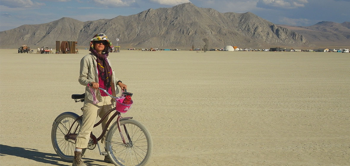 Professor Carolyn White poses for a photo with her bike on the Playa at Burning Man