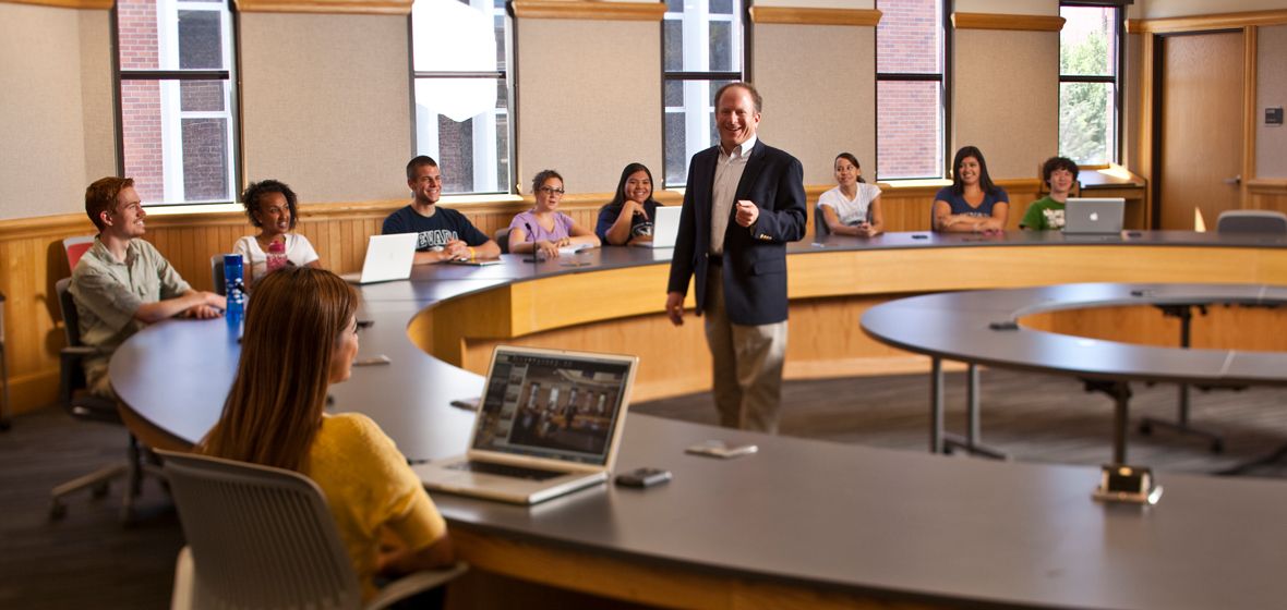 A man stands in the center of a classroom surrounded by students. 