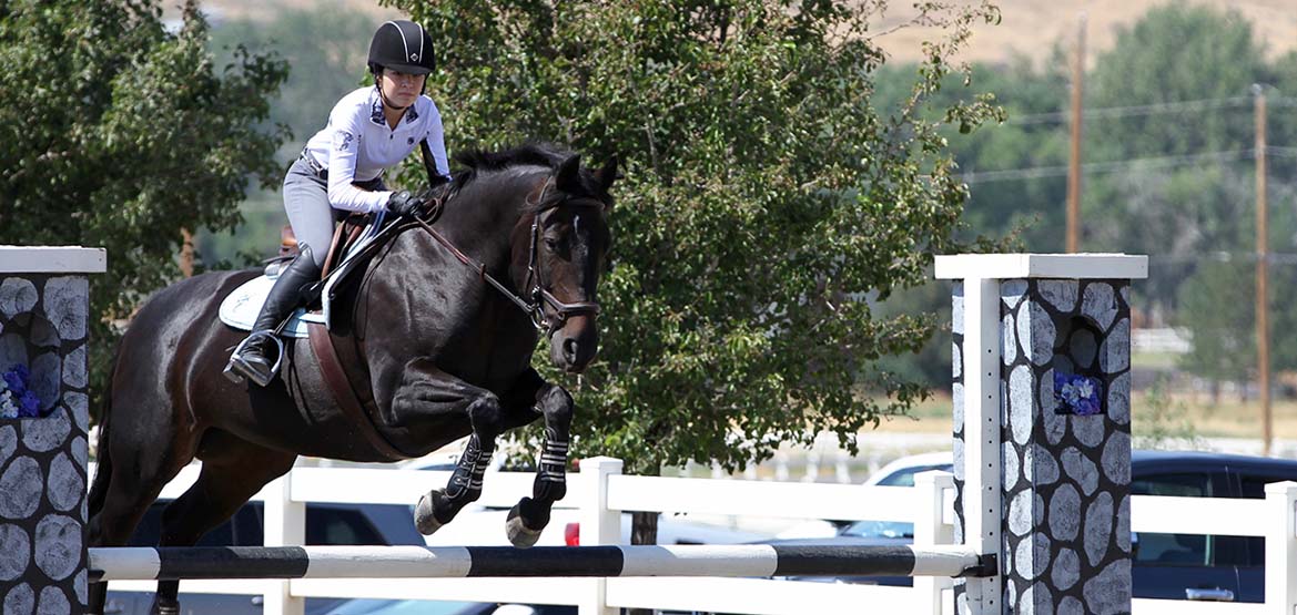 Girl riding a horse as the horse clear a jump