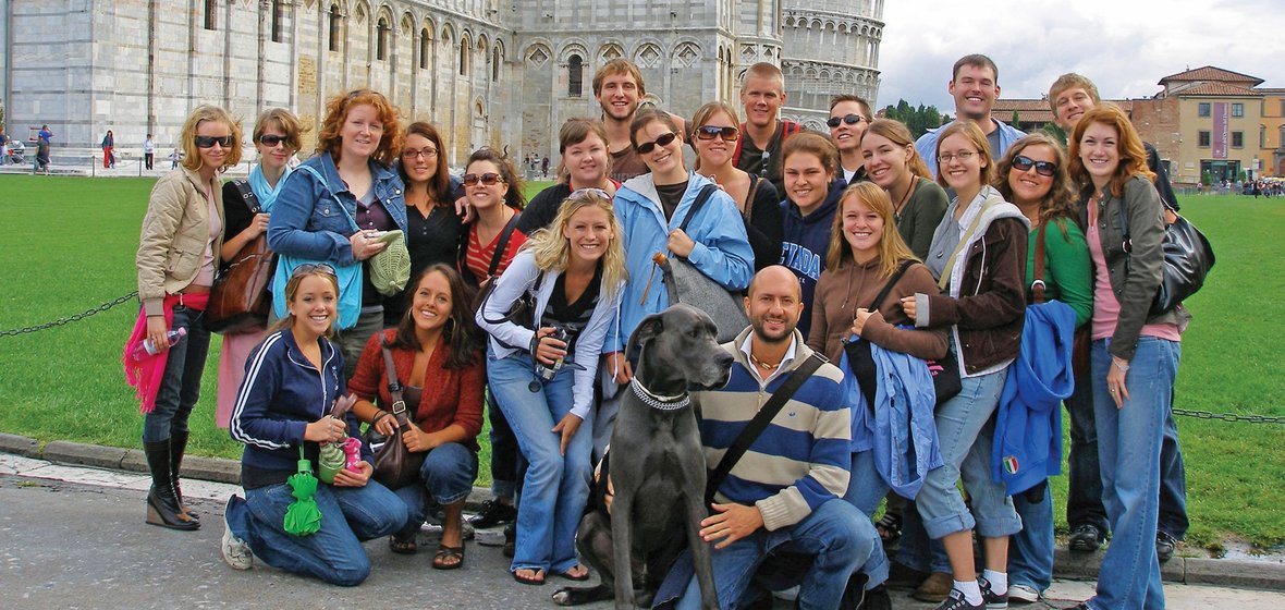 University students and faculty posing on a lawn in Italy with the Leaning Tower of Piza and other classic architecture in background