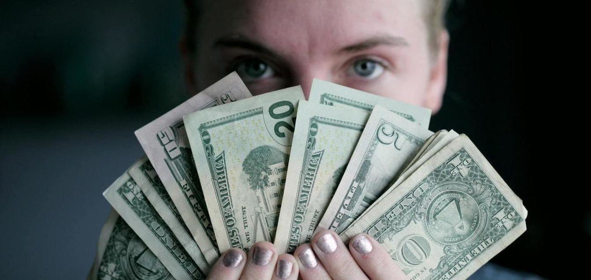Woman holding fanned out cash in front of her face