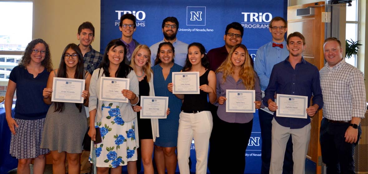 McNair Scholars and their mentors standing in front of a TRiO Programs banner hold up certificates