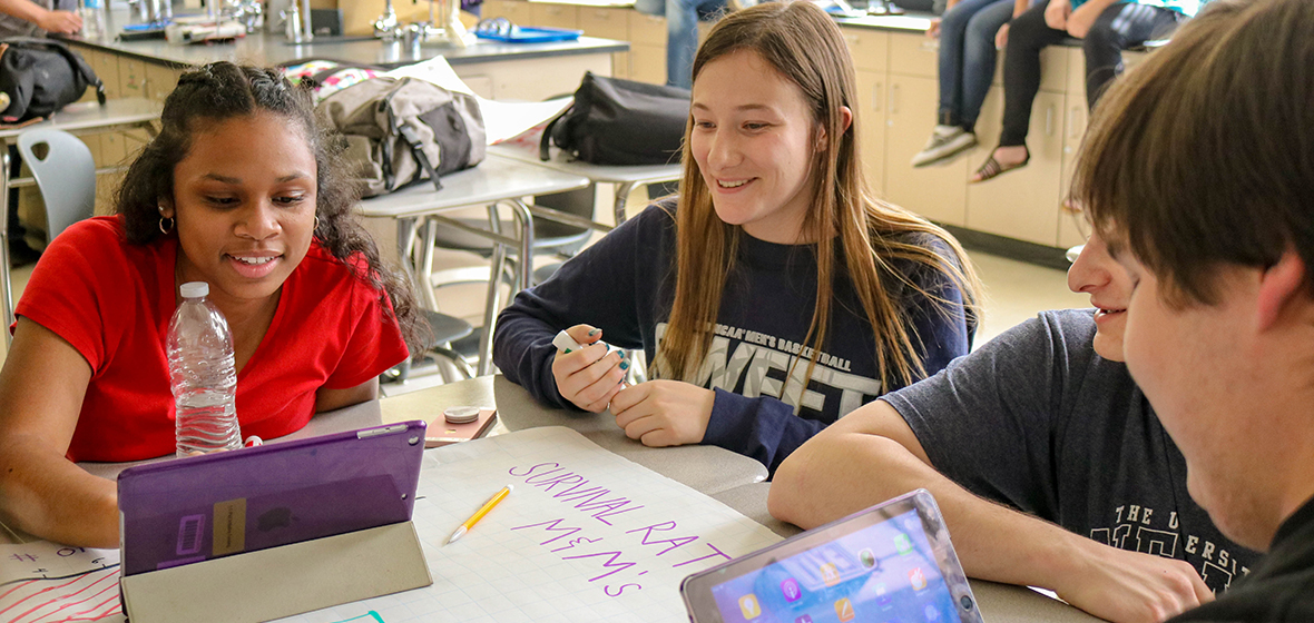 Student teacher sitting at table with two students looking at iPads