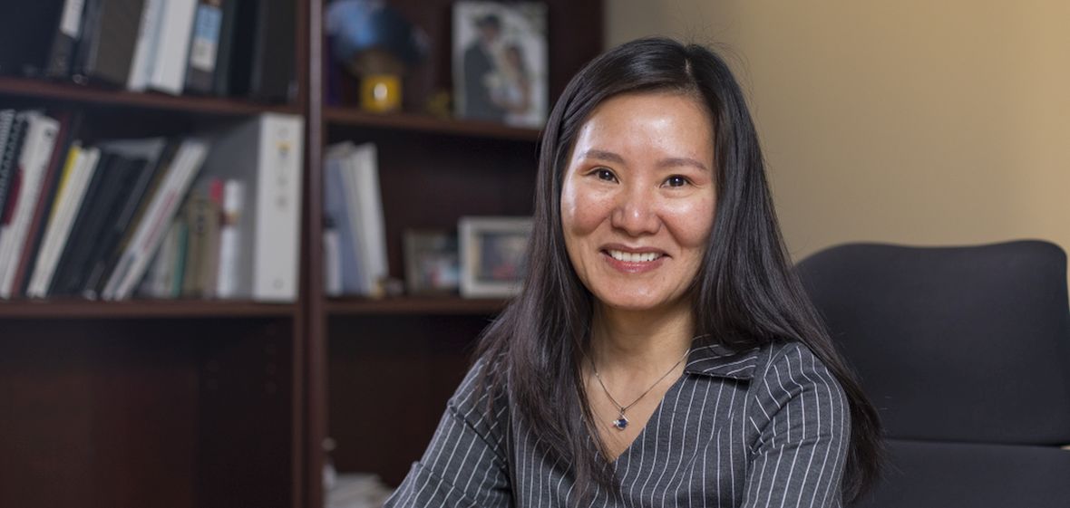 Dr. Yumei Feng sitting in her office with book shelves in the background