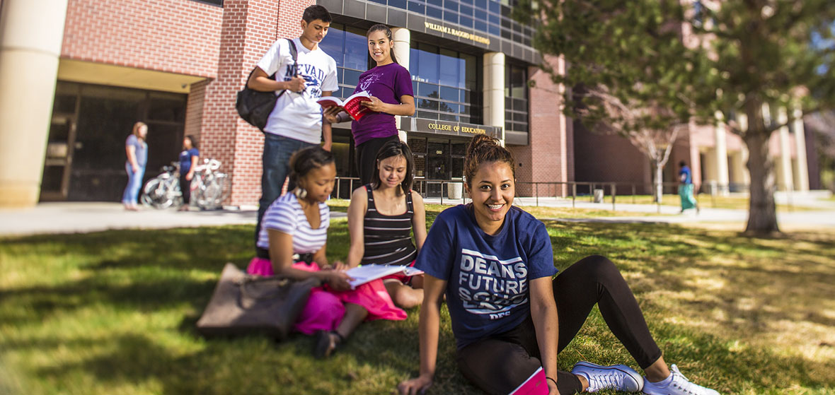 Photo of students - two standing and three sitting - in front of the William Raggio Building on campus.