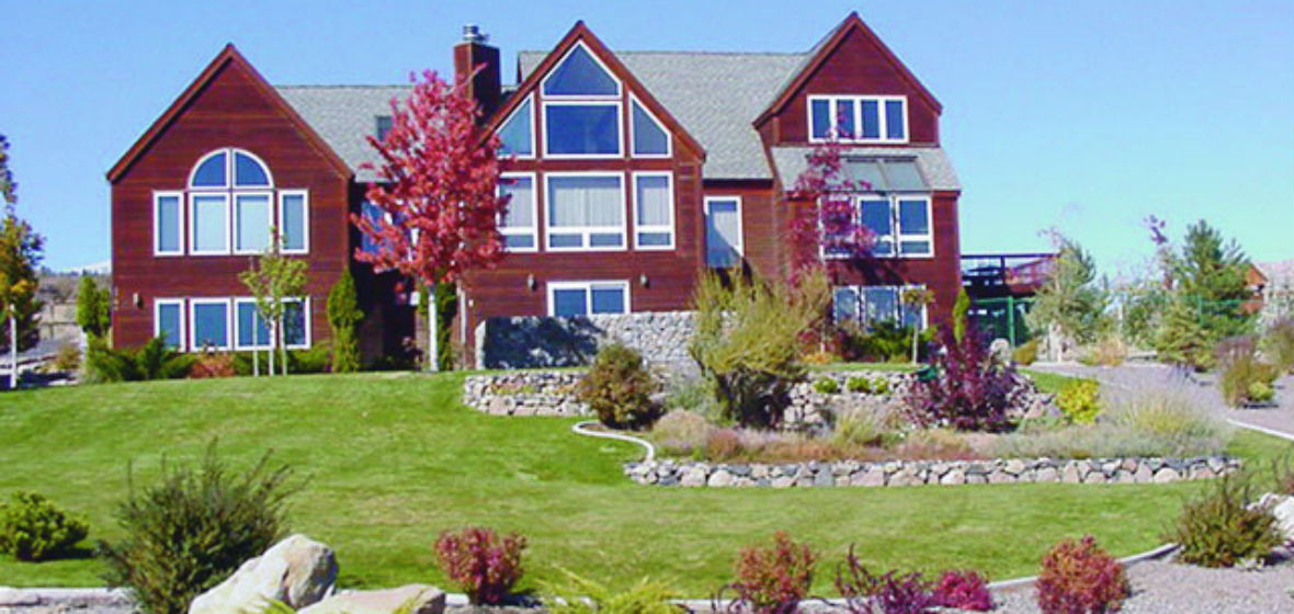 Two-story house with lawn, deciduous trees and small bushes