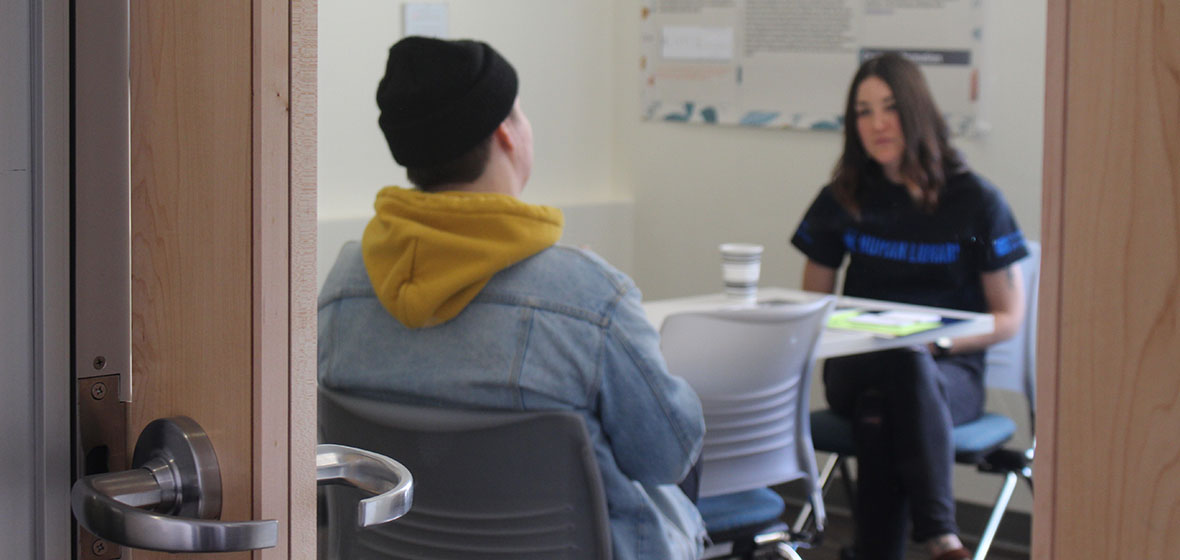 A human book is speaking to a reader in a room in the Writing Center. 