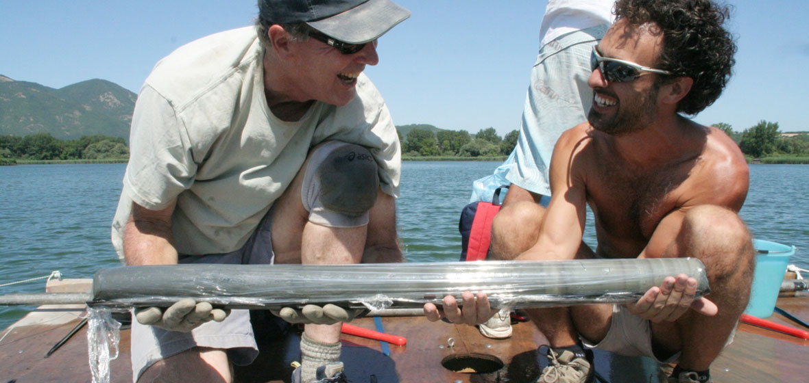 Two men on a boat smiling at each other and holding a core