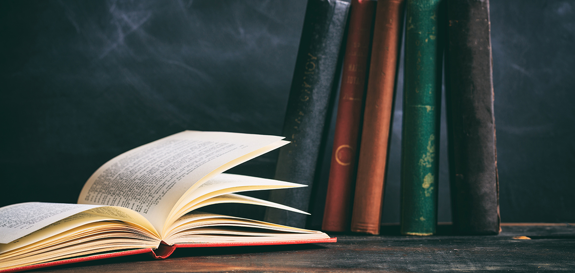 Book open on table with vintage books standing up in front of blackboard