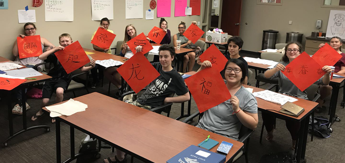 Students sit in classroom while holding up red papers with Chinese calligraphy