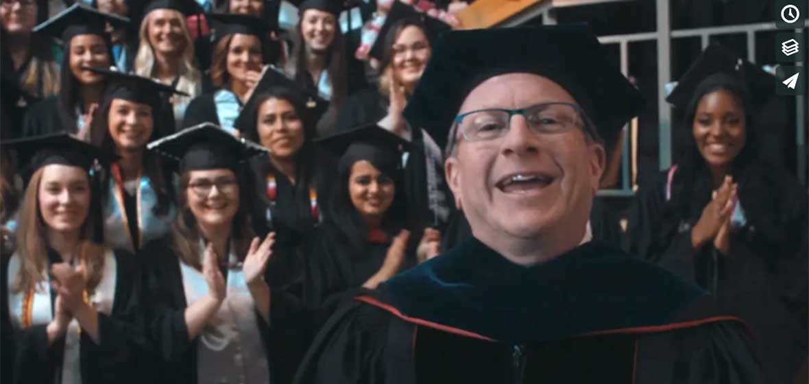 A man in a graduation robe in front of a crowd of graduation robes. 