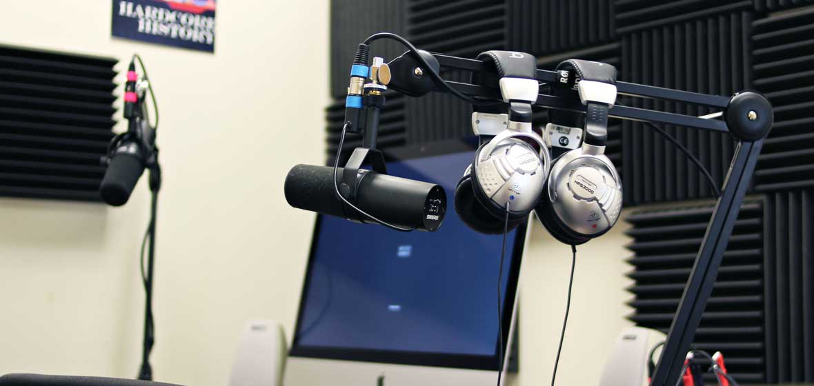 A small editing studio, where two pairs of headphones are seen hanging off of a microphone. 