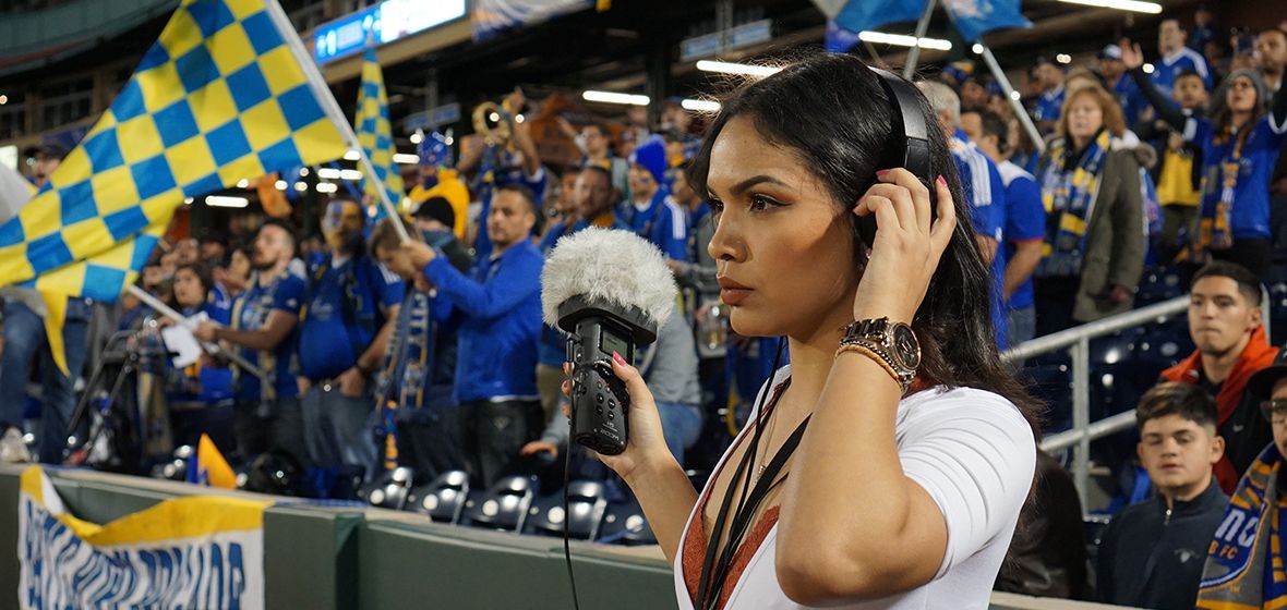 Woman stands with headphones and a microphone in front for a crowd of people.