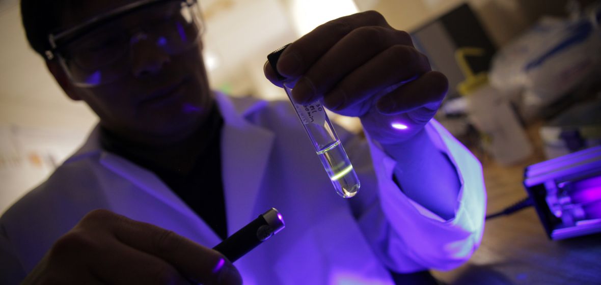Researcher shines light on a test tube in a darkened lab