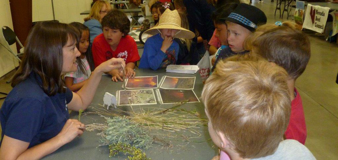 Presenter explaining vegetation photos and samples to five elementary students