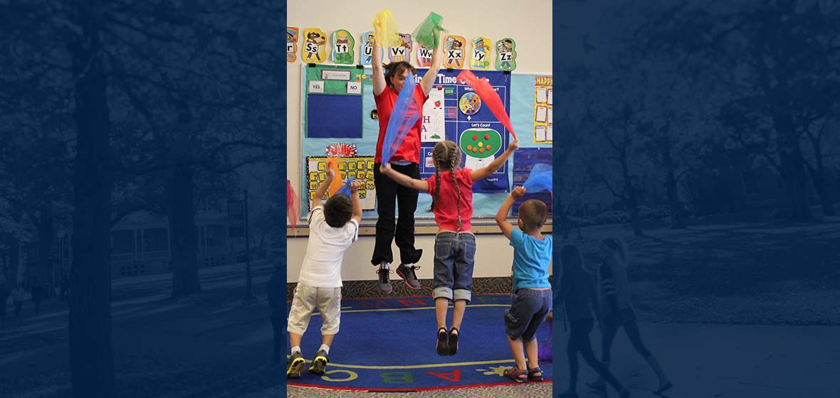 A teacher and elementary kids jumping while waving colorful scarves