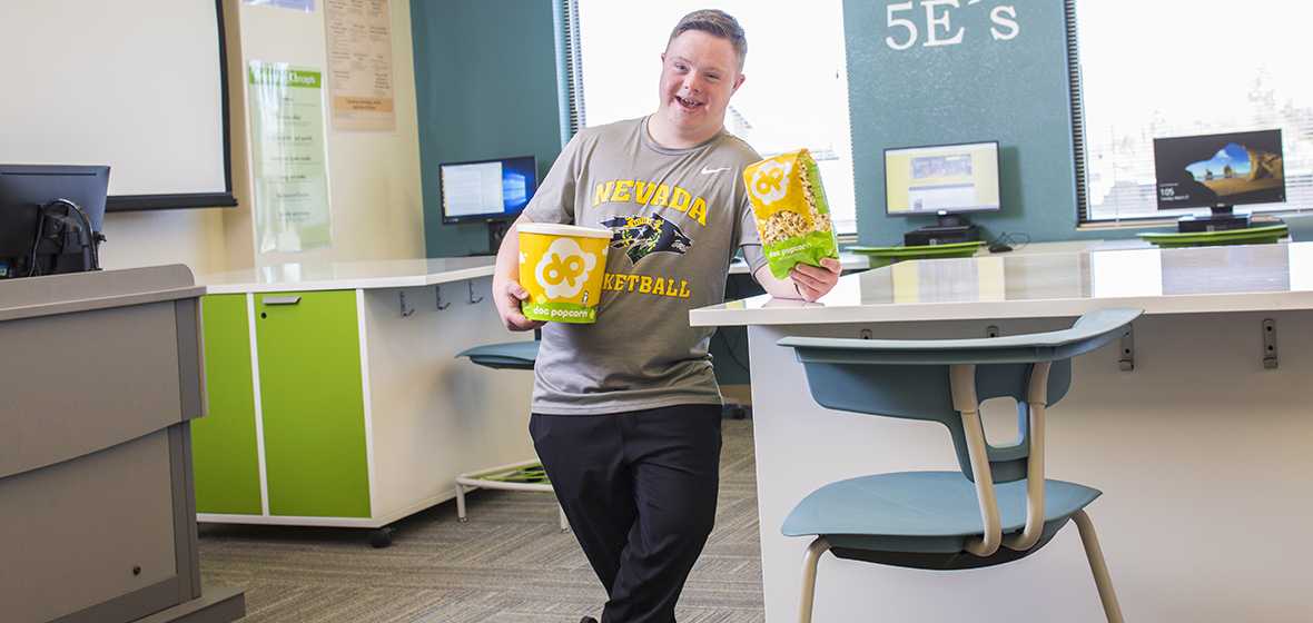 Jack Rovetti leaning against a table while holding two bags of popcorn.