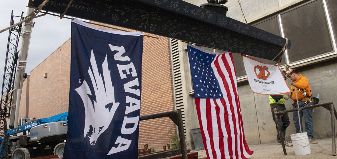 The flags of the Nevada Wolf Pack, United States of America and Q&D Construction hang from a steel beam.