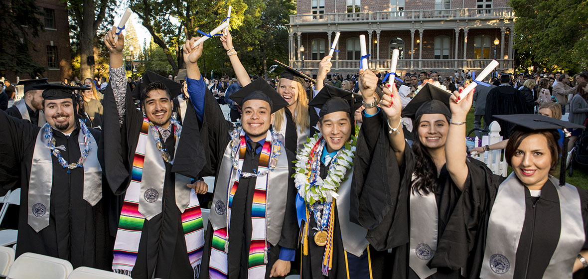 Graduates hold up their diplomas in front of Morill Hall