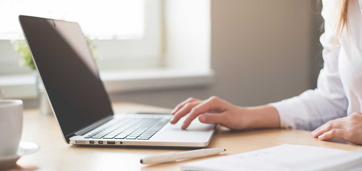 A hand can be seen typing at a laptop. 