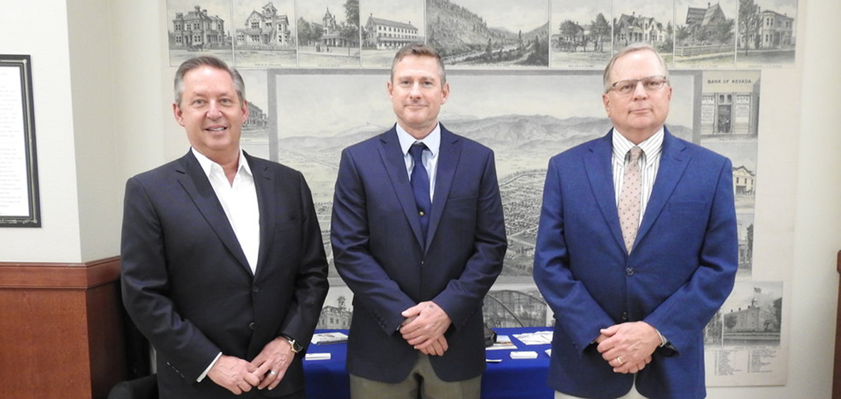 Chip Bowlby, Brian Bonnenfant and J. Carter Witt III stand alongside each other in front of a mural in the library. 