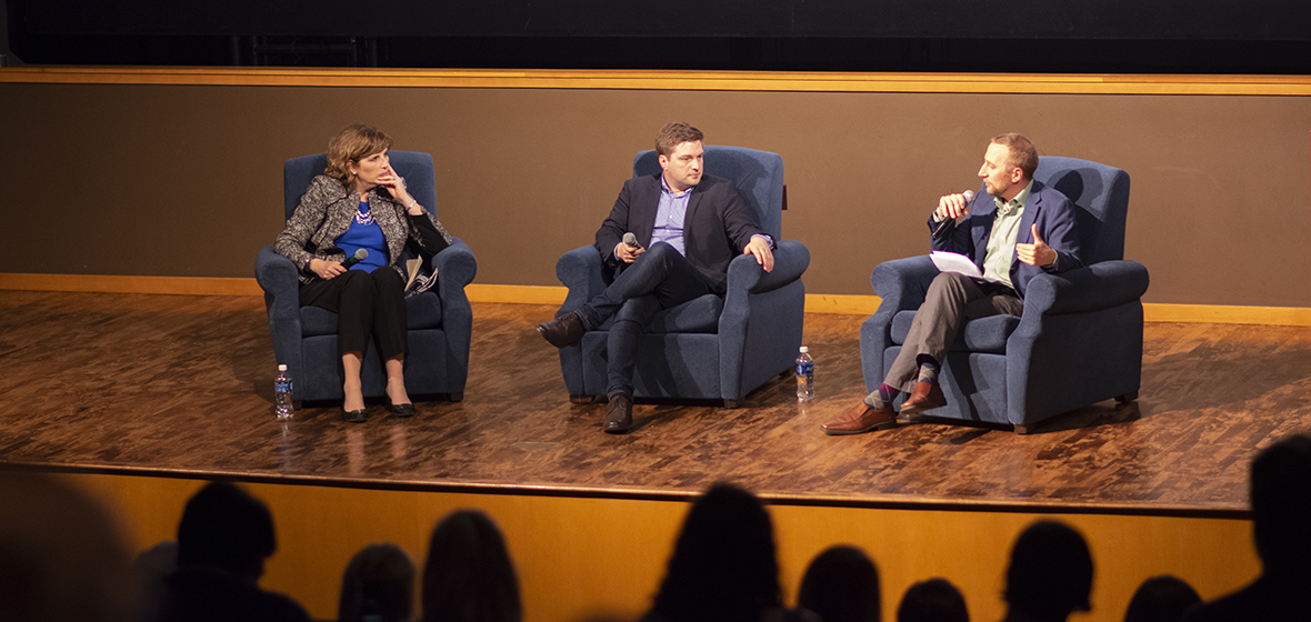 Three people sit on stage. 