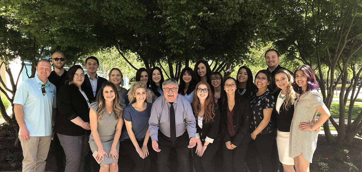 Students pose with professor outdoors in front of trees.