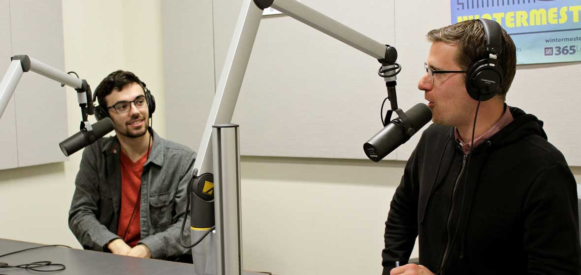 Two men sit in a recording studio. 