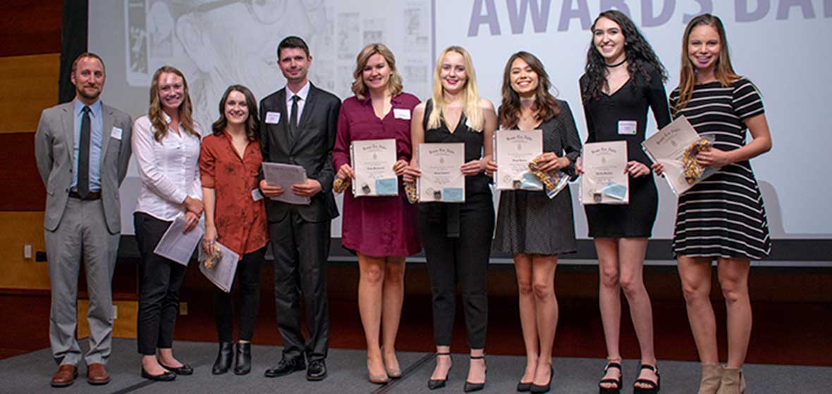 A group of students stand on a stage, all holding awards. 
