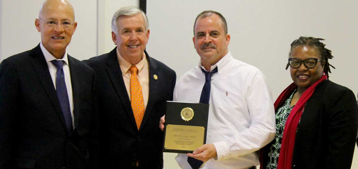 A group of people pose for the camera, with one man holding an award. 