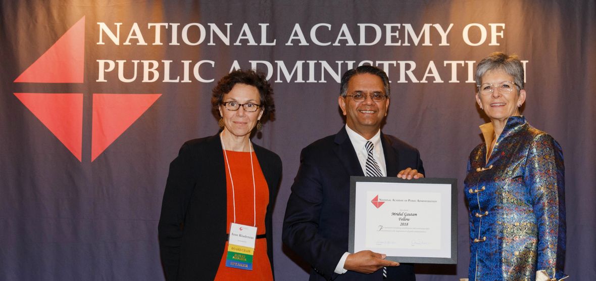 Two National Academy of Public Administration representatives present Mridul Gautam with a framed recognition of his induction.