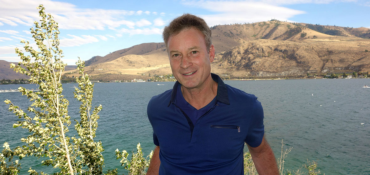 Man stands outdoors with a lake behind him.