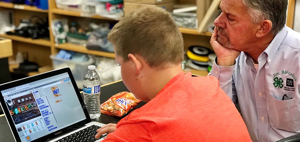 man wearing a 4H shirt helping boy with coding program on laptop