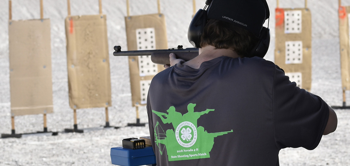 a boy with a 4-H shooting sports shirt shoots a rifle at a target