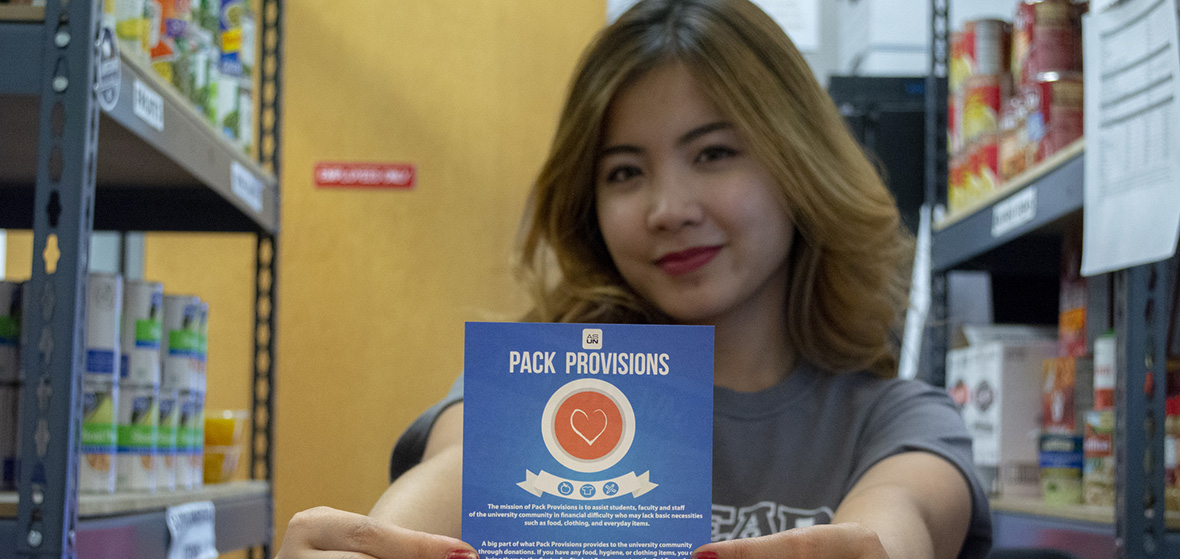 Student worker inside Pack Provisions holding out one of the Pack Provisions fliers