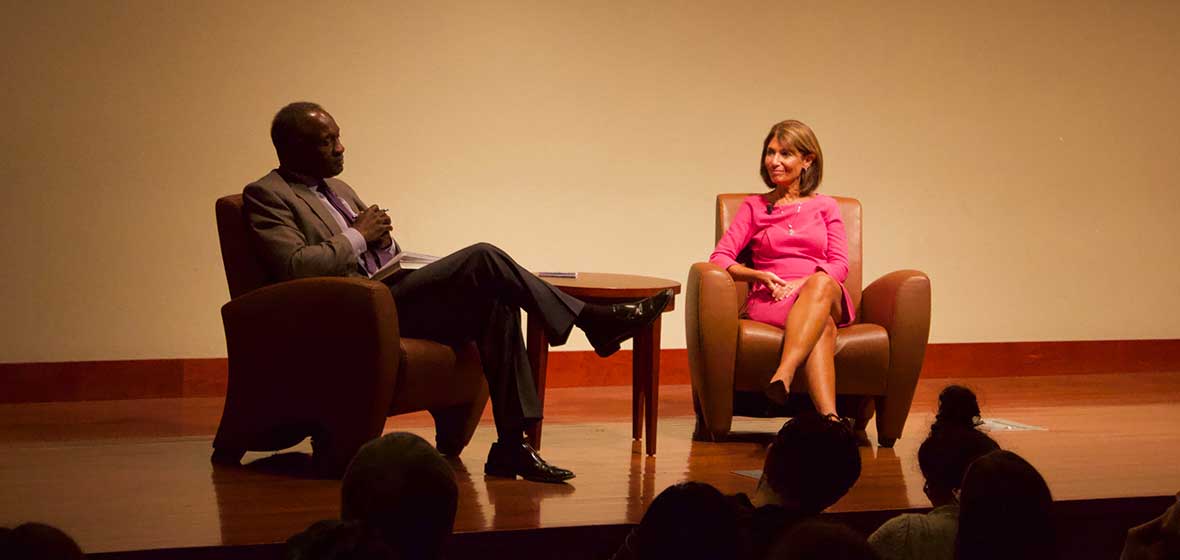 Two people sit in armchairs on a stage.