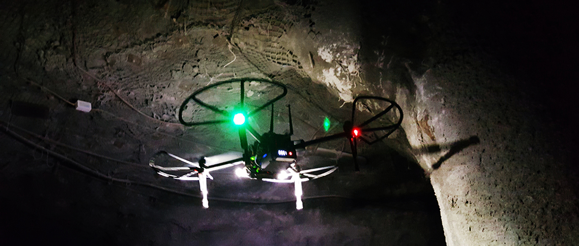 aerial robot with green and red lights flies in a darkened mine