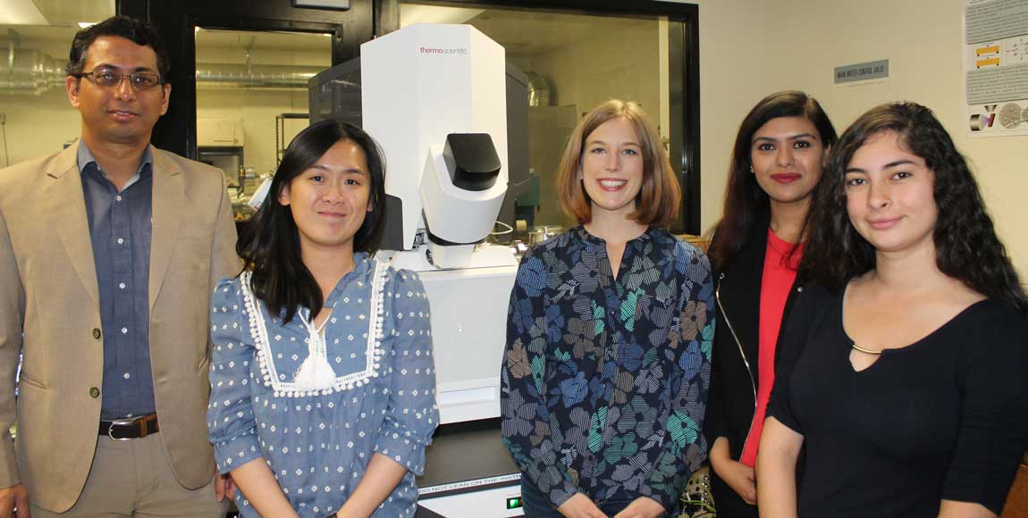 A research group stands in front of a machine.