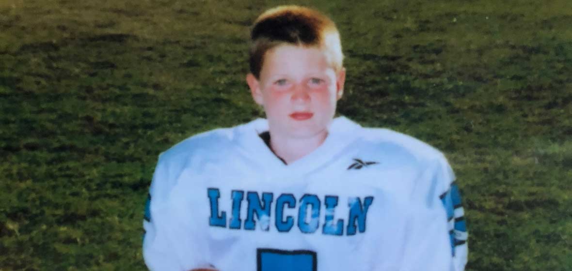 A young boy wearing a football jersey poses with a football.